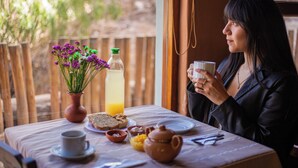 A dining table with a meal, a cup, and a vase of flowers. - Don Juan posada andina (Tilcara)