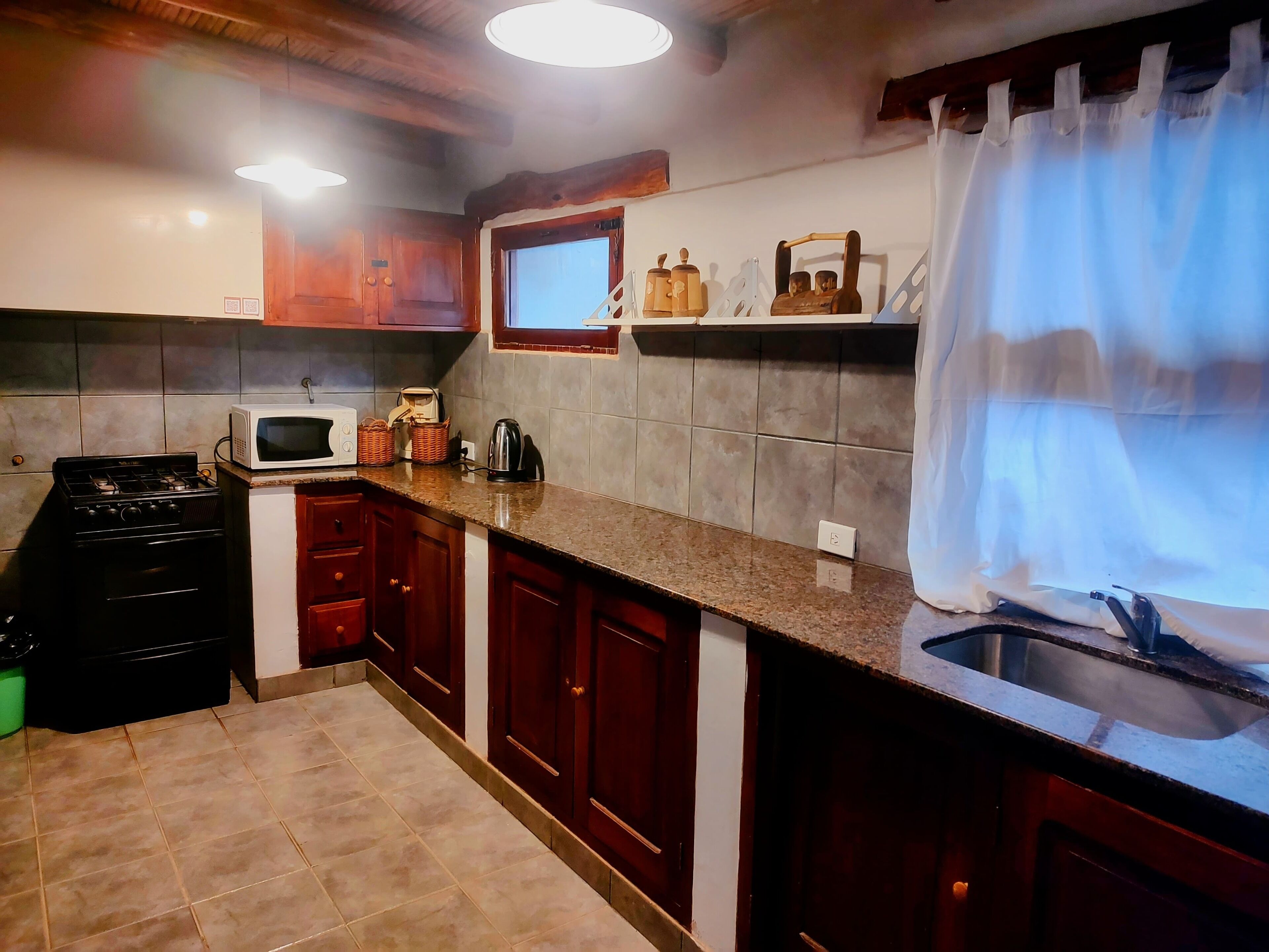 Une cuisine avec des meubles de rangement en bois, une cuisinière à gaz, un four à micro-ondes et une fenêtre avec un rideau.