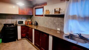 Una cocina con armarios de madera, estufa a gas, microondas y una ventana con cortina.