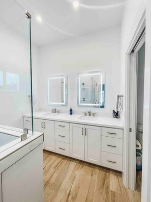 Een moderne badkamer met twee wasbakken, een douchecabine met glazen wanden en een houten vloer.