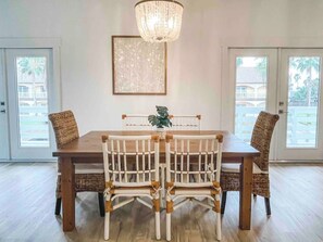 Een eethoek met een houten tafel en twee witte stoelen met houten details. Daarboven hangt een kroonluchter en aan de muur hangt een kunstwerk in een lijst.