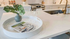 A kitchen counter with a tray holding a magazine, a vase with a plant, and three glasses. - Pearl House - Heated Pool & Hot Tub, Sleeps 20! (South Padre Island)