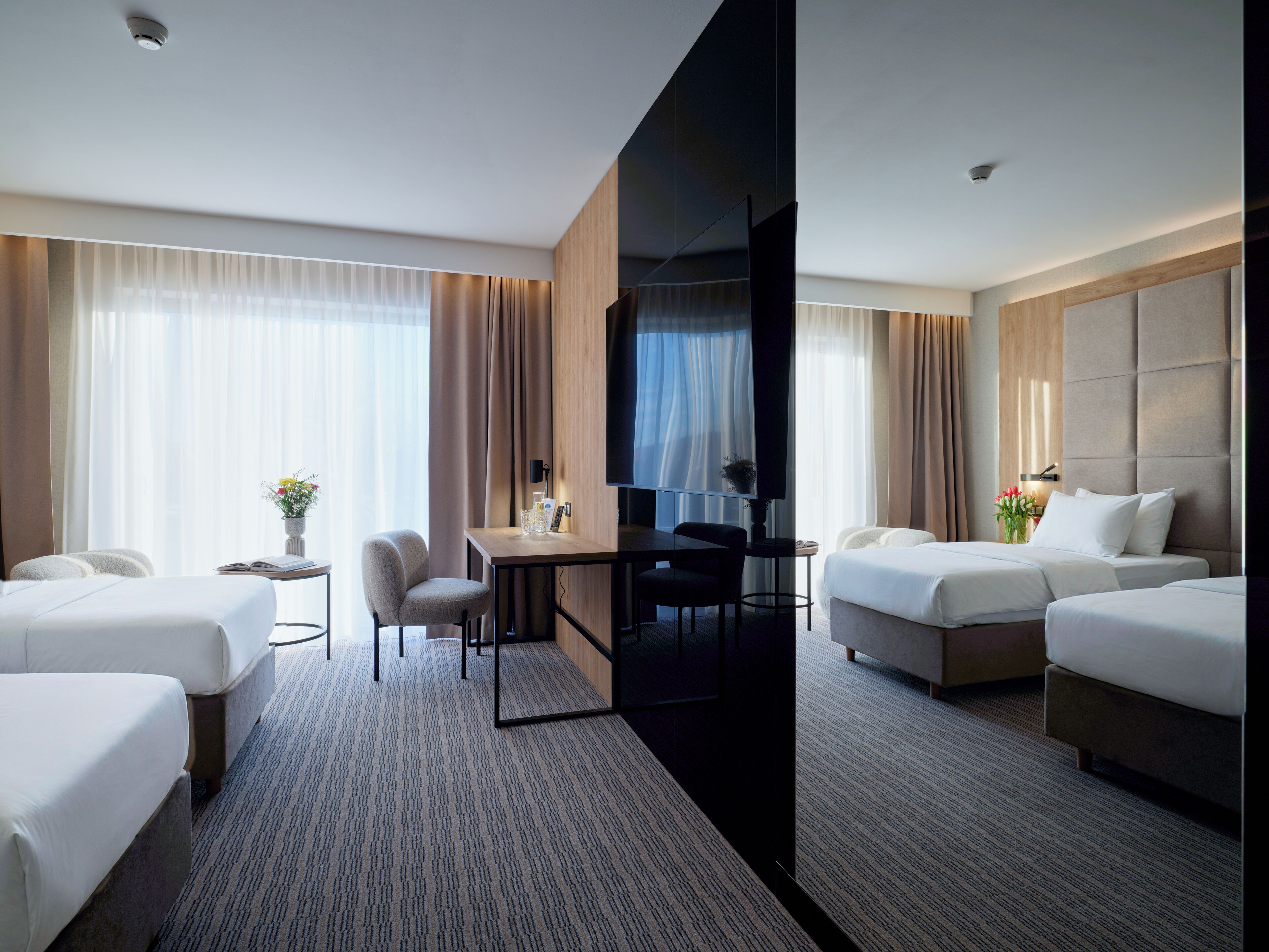 A hotel room with two beds, a desk, a chair, and a TV.
