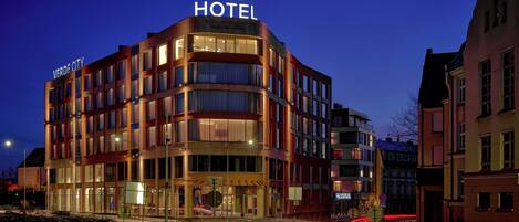 A modern hotel with a prominent "HOTEL" sign, multiple floors, and a well-lit facade.