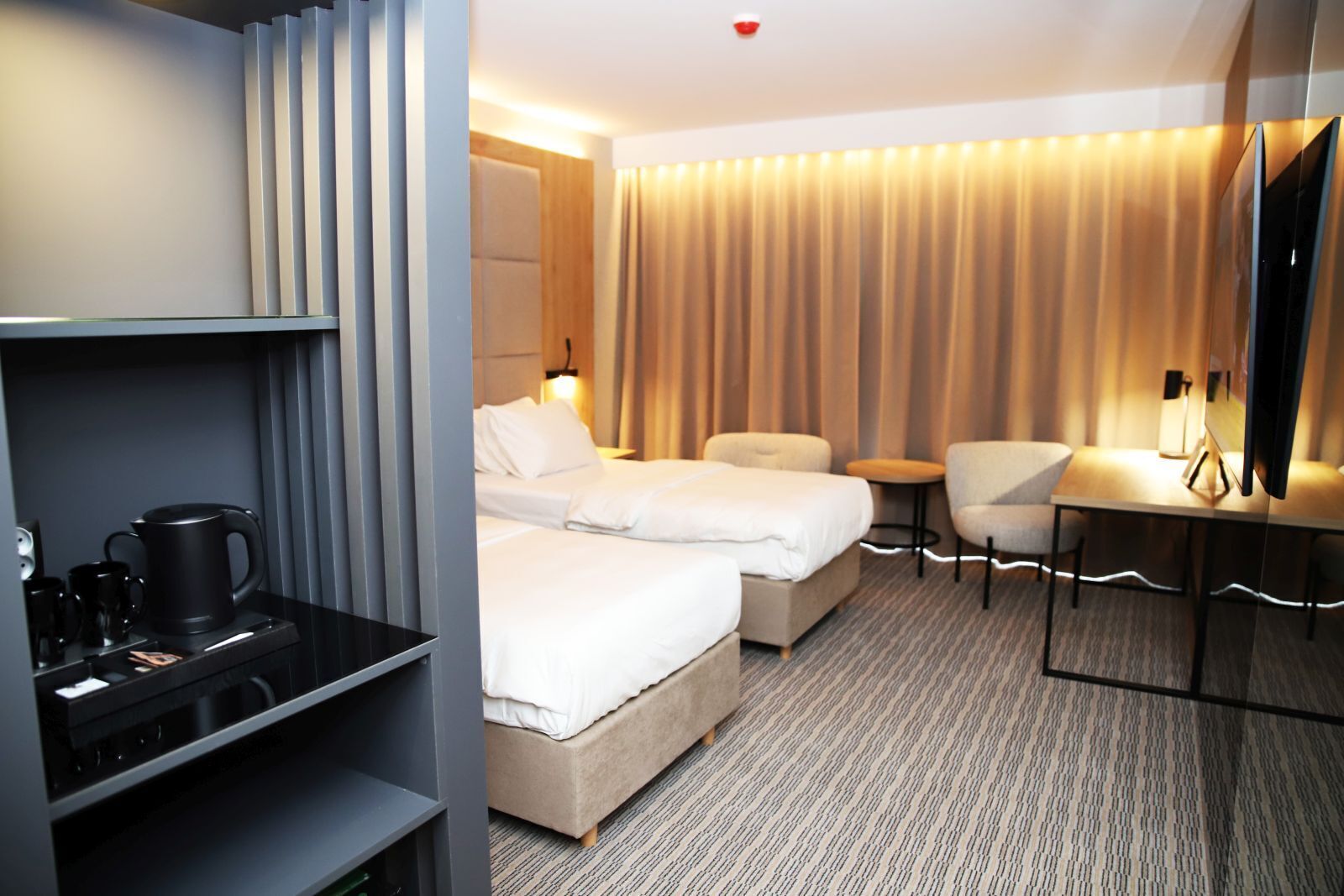 A hotel room with two beds, a desk, a chair, and a minibar.