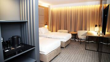 A hotel room with two beds, a desk, a chair, and a minibar.