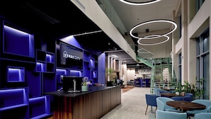 A modern reception area with a dark wood reception desk, a sign reading "VERDECITY", and a staircase leading to an upper level.