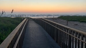En träpromenad som leder till en strand, med en solnedgång i bakgrunden.