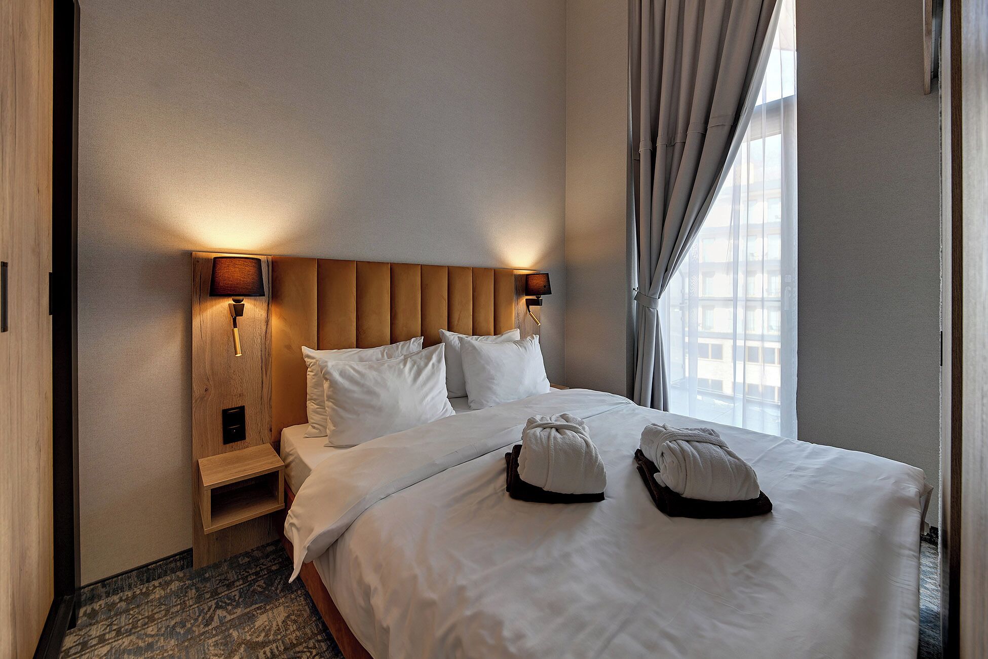 Hotelkamer met een groot bed, twee bedlampen, een houten hoofdeinde en uitzicht op de stad door het raam.