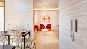 Una sala de estar moderna con comedor, que incluye un sofá, sillas rojas, una mesa de centro y un cuadro en la pared.