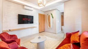 Una sala de estar moderna con una televisión de pantalla plana, sofás rojos, una mesa de centro blanca y una lámpara de techo original.
