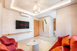 A modern living room with a flat-screen TV, red sofas, a white coffee table, and a unique ceiling light fixture. - Cozy 2-Bedroom Apartment in Marrakech City Center (Marrakech)