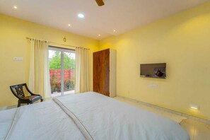 Ein Hotelzimmer mit einem großen Bett, einem Holzschrank, einem an der Wand befestigten Fernseher und einem Fenster mit Vorhängen.
