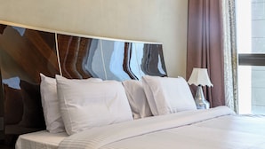 A neatly made bed with white linens, a dark headboard, and a small bedside table with a lamp. - Vesta - Luxury Apt- 1br- Aeon Tower (6th of October City)