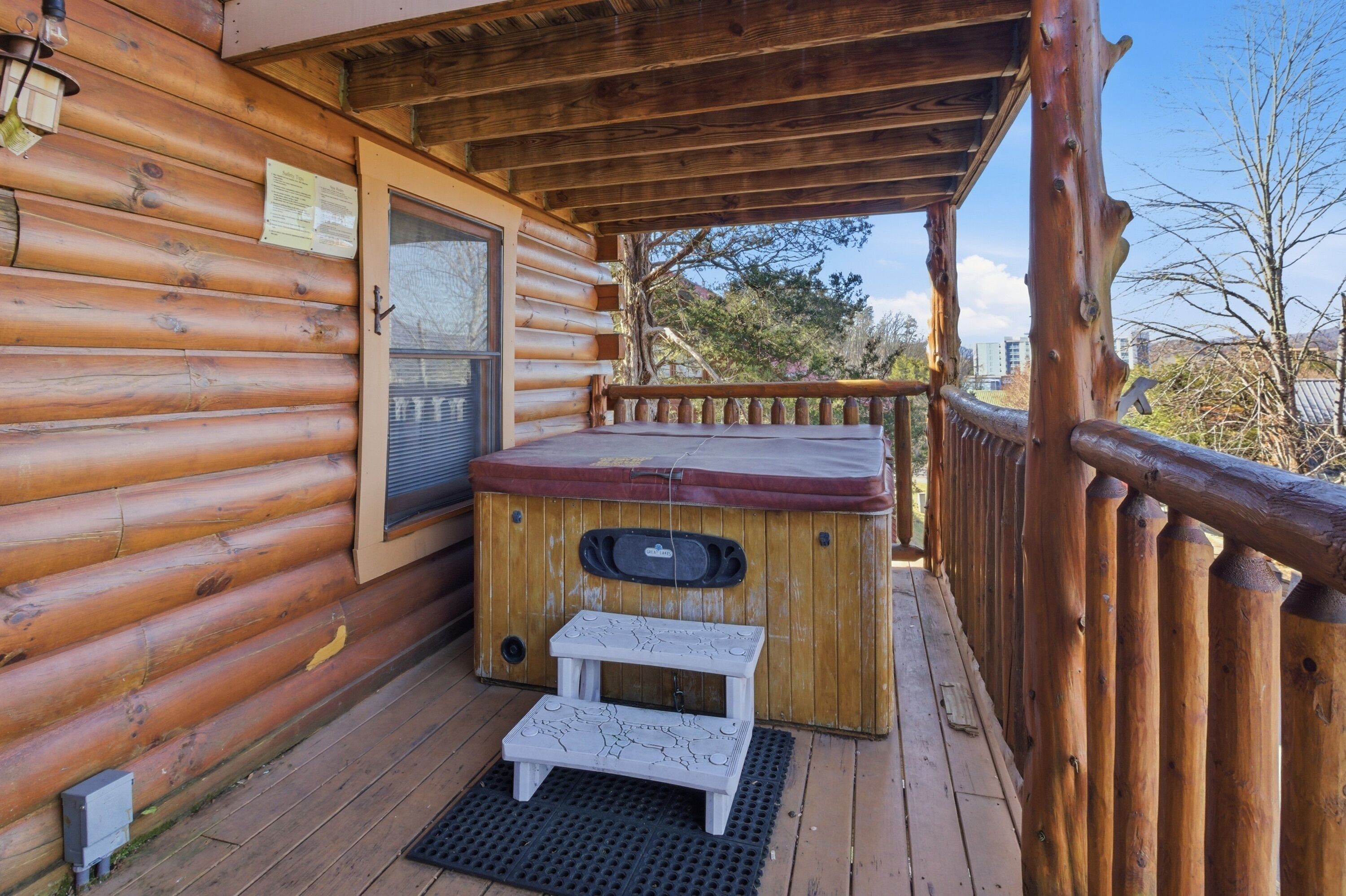 A log cabin with a wooden deck, a hot tub, and a small step stool.