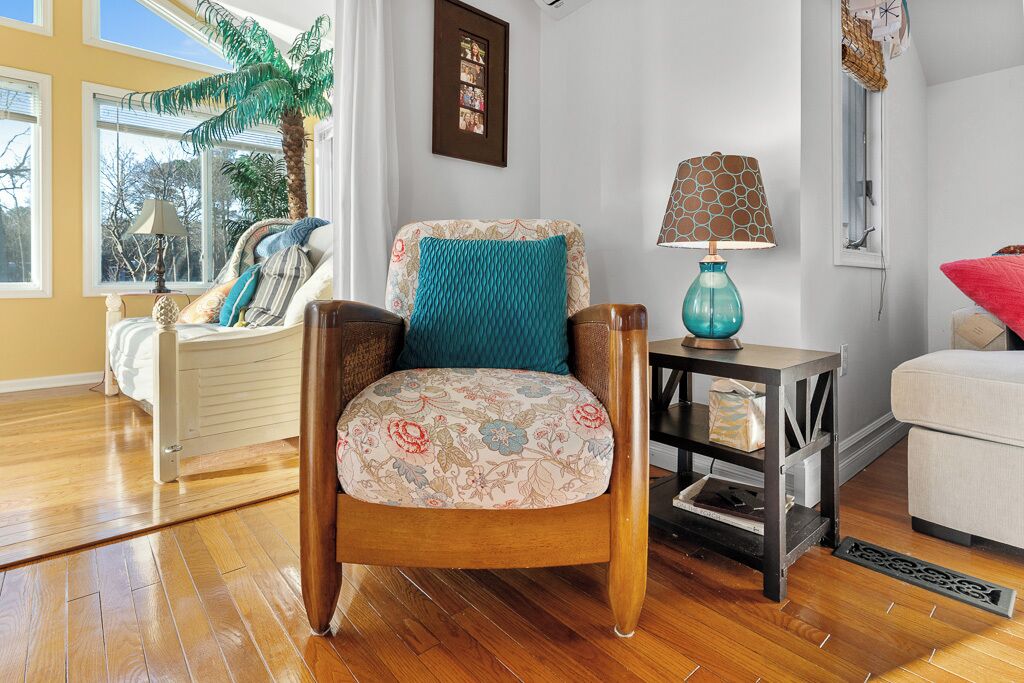 Un salon avec un fauteuil en bois, une table d’appoint avec une lampe et un canapé.