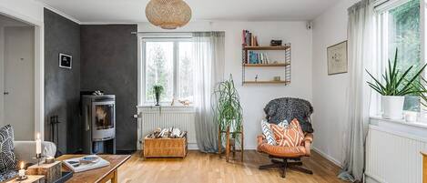 A cozy living room with a fireplace, a wooden coffee table, a comfortable armchair, and a bookshelf.