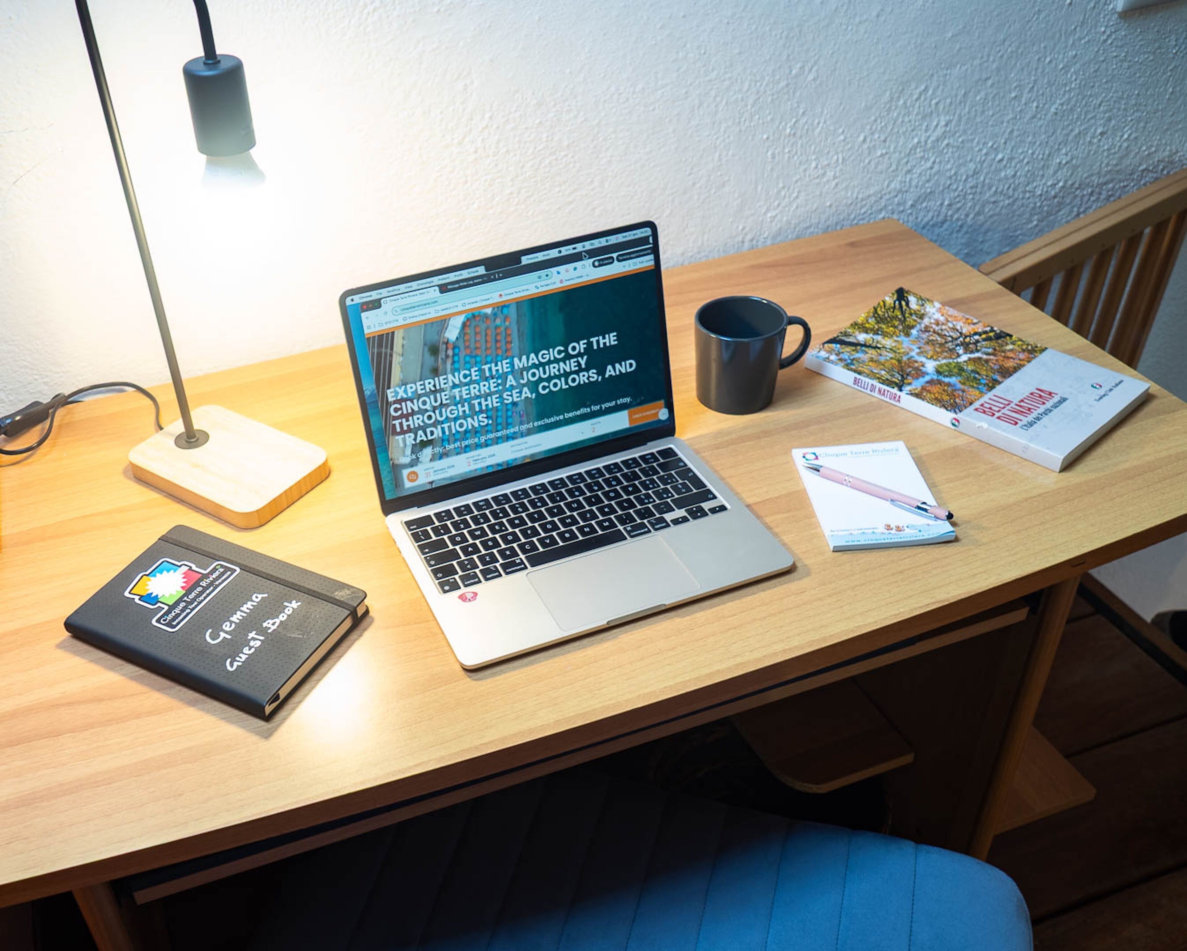 A laptop on a wooden desk with a book, a mug, and a notebook.