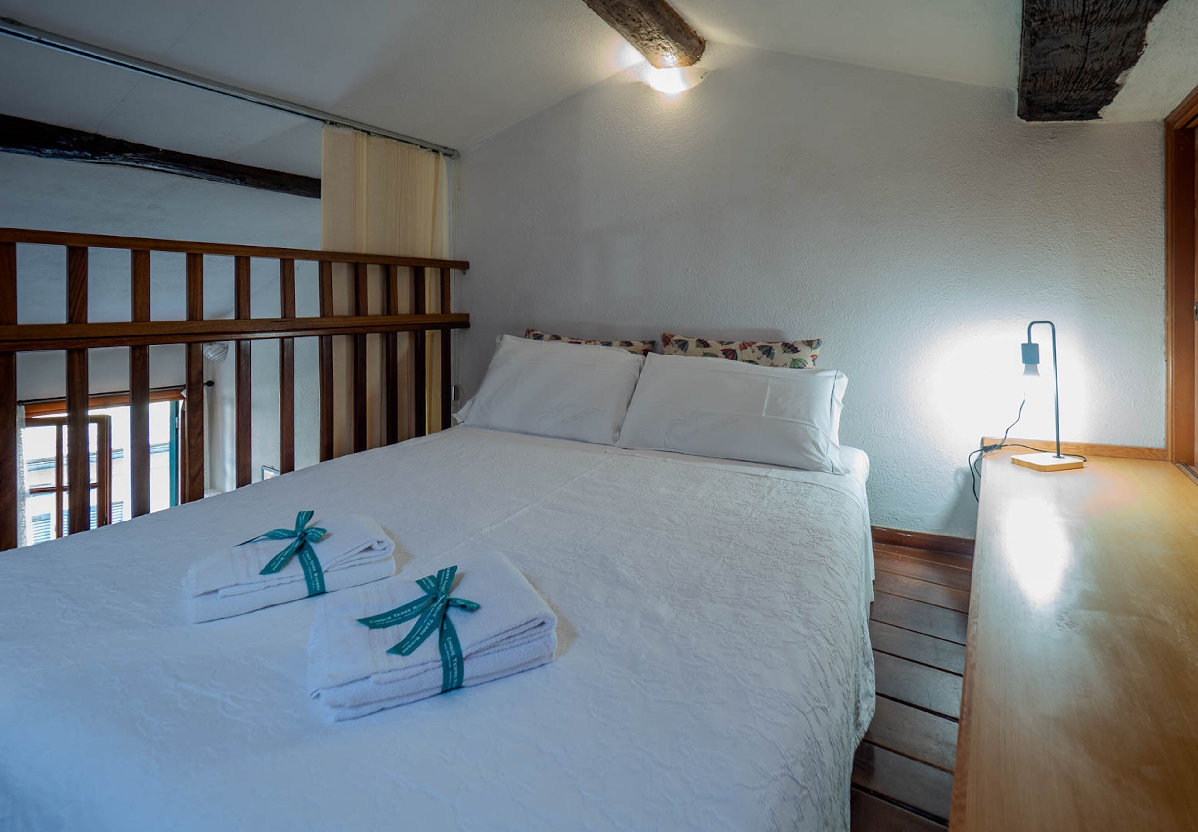 Una cama bien tendida con ropa de cama y toallas blancas, un cabecero de madera y una mesita de noche con una lámpara.