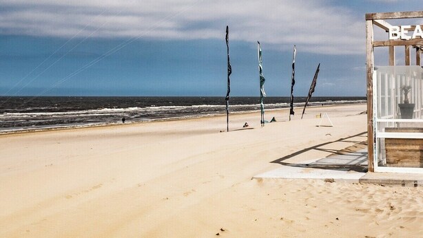 A beach with a parasail in the air, a wooden structure labeled "BEACH", and several flags on poles. - Cottage Strand & Centrum @NoordwijkMeer.nl (Noordwijk)
