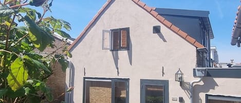 A two-story house with a sloped roof, a balcony, and a small garden area with a rose bush.