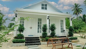 A white colonial-style building with a front porch, steps leading to the entrance, and a wooden bench outside.