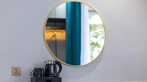 A modern room with a desk, a chair, a round mirror, and a coffee maker.