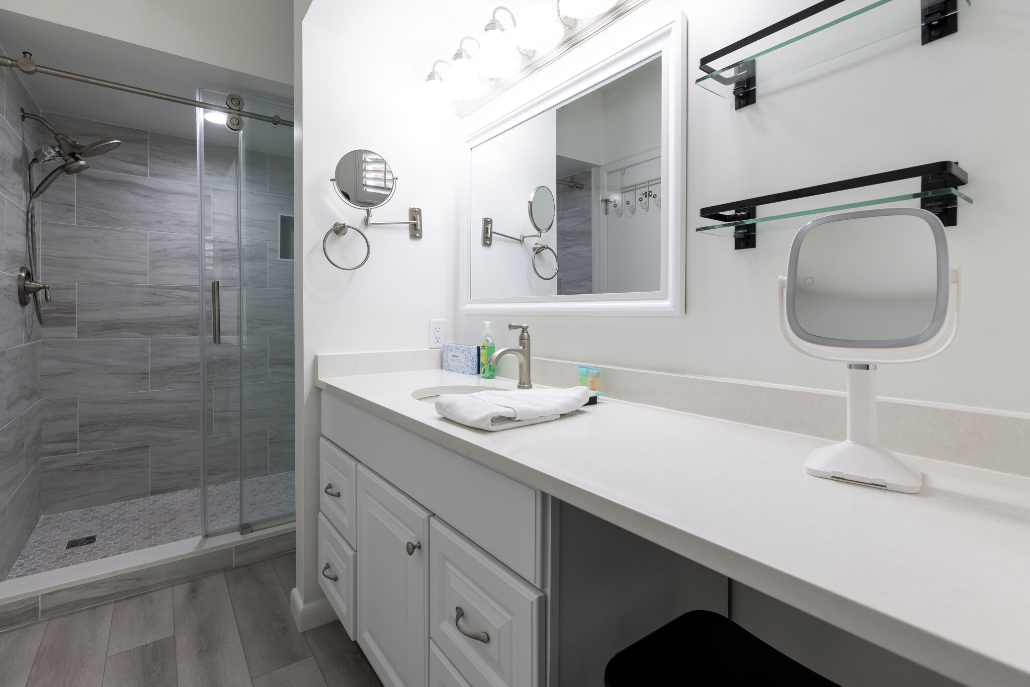 A modern bathroom with a glass shower enclosure, white vanity with a mirror, and a towel rack.
