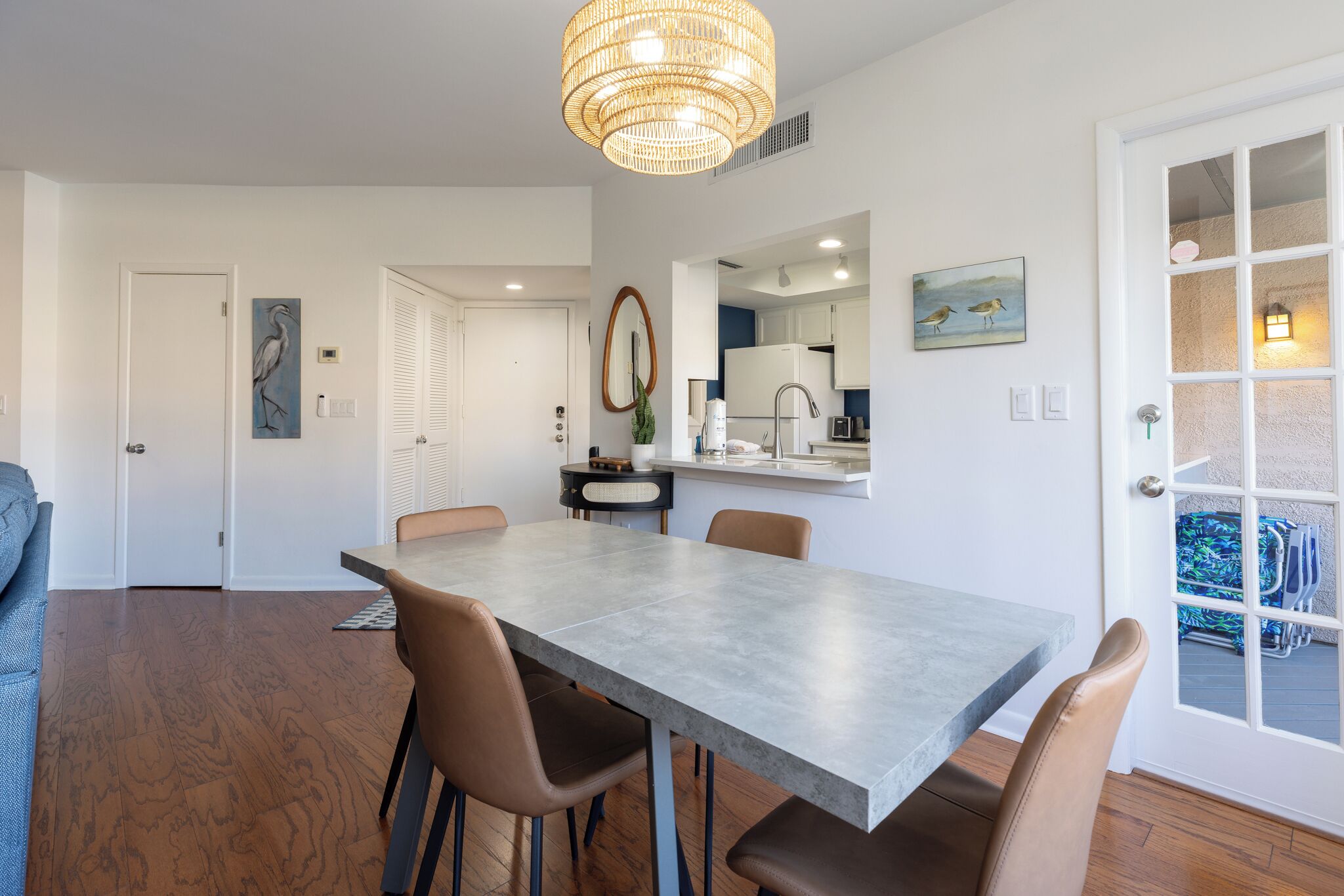 A modern dining area with a large table and chairs, a chandelier, and a view of the kitchen and outdoor seating area.