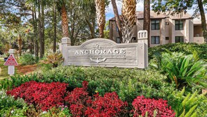 A sign for 'The Anchorage at Shelter Cove' with a no bicycles or pedestrians on pavement sign, surrounded by lush greenery and palm trees. - 7447 Anchorage: Pet Friendly 2 Bedroom Villa with Water Views, Sleeps 6 (Hilton Head Island)