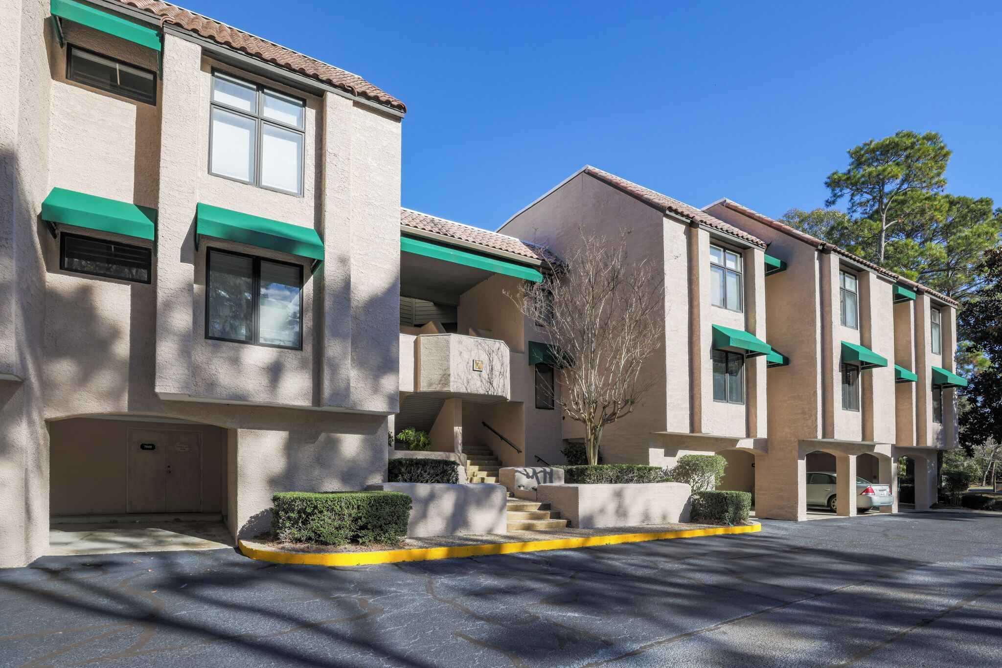 A multi-story building with a beige exterior, green awnings, and a parking area with a yellow curb.