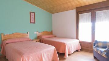 Una habitación con dos camas individuales, cabeceros de madera, techo de madera, una ventana con persianas y un sofá con funda a cuadros.