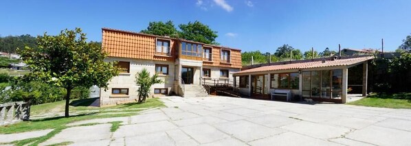 Ein zweigeschossiges Haus mit einem Ziegeldach, einer überdachten Terrasse und einem gepflasterten Einfahrt.
