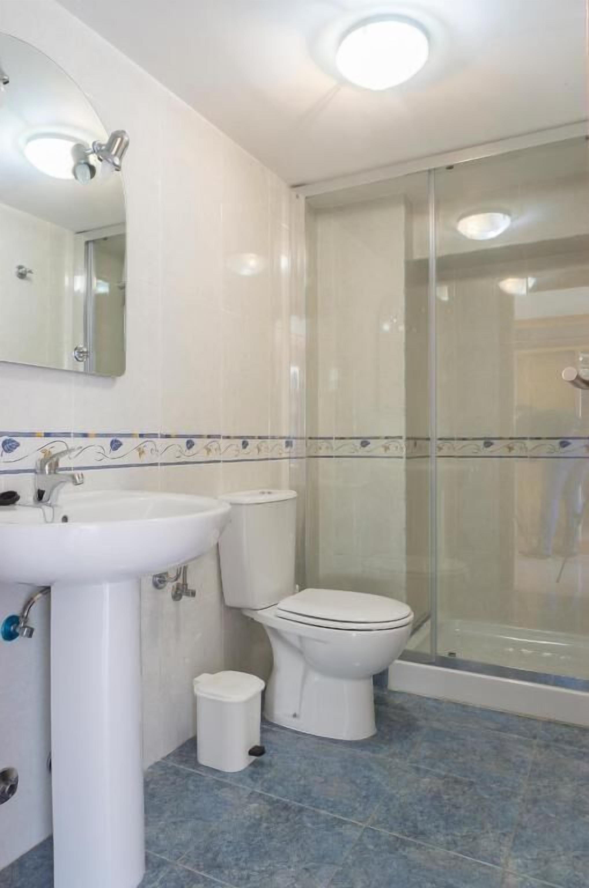 Un baño con lavamanos blanco, inodoro y cabina de ducha con mampara de vidrio.