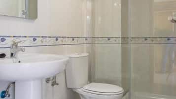 Un baño con lavamanos blanco, inodoro y cabina de ducha con mampara de vidrio.
