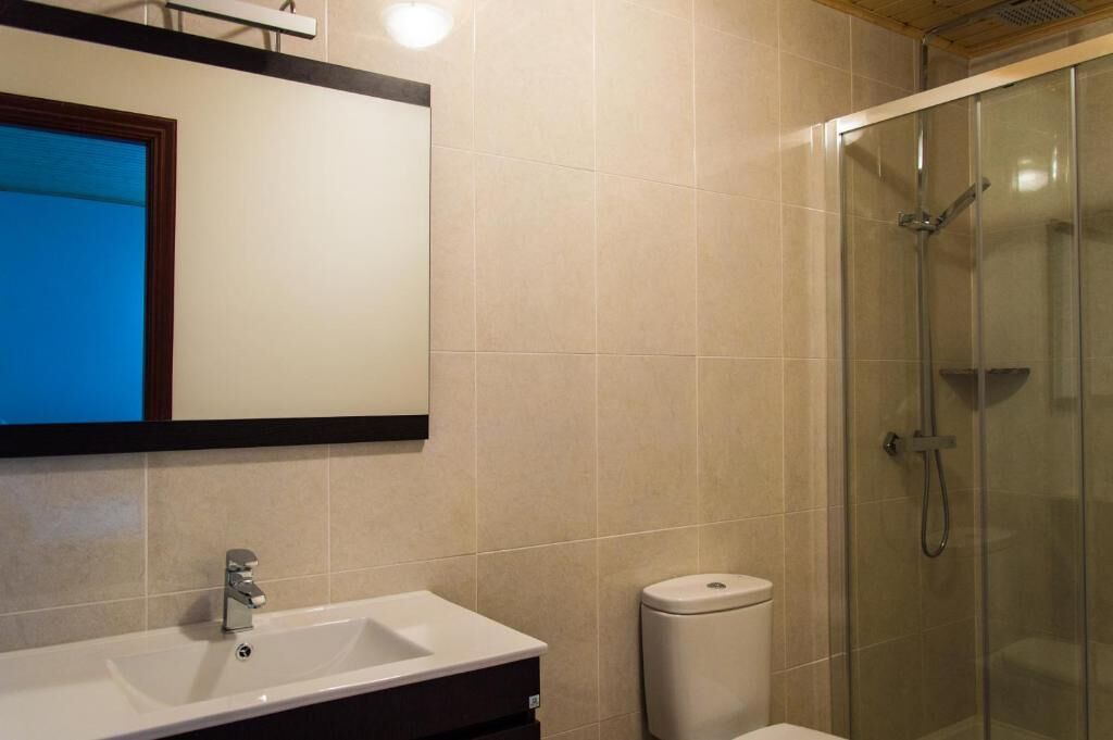 Baño con lavamanos, espejo, inodoro y ducha con mampara de vidrio.