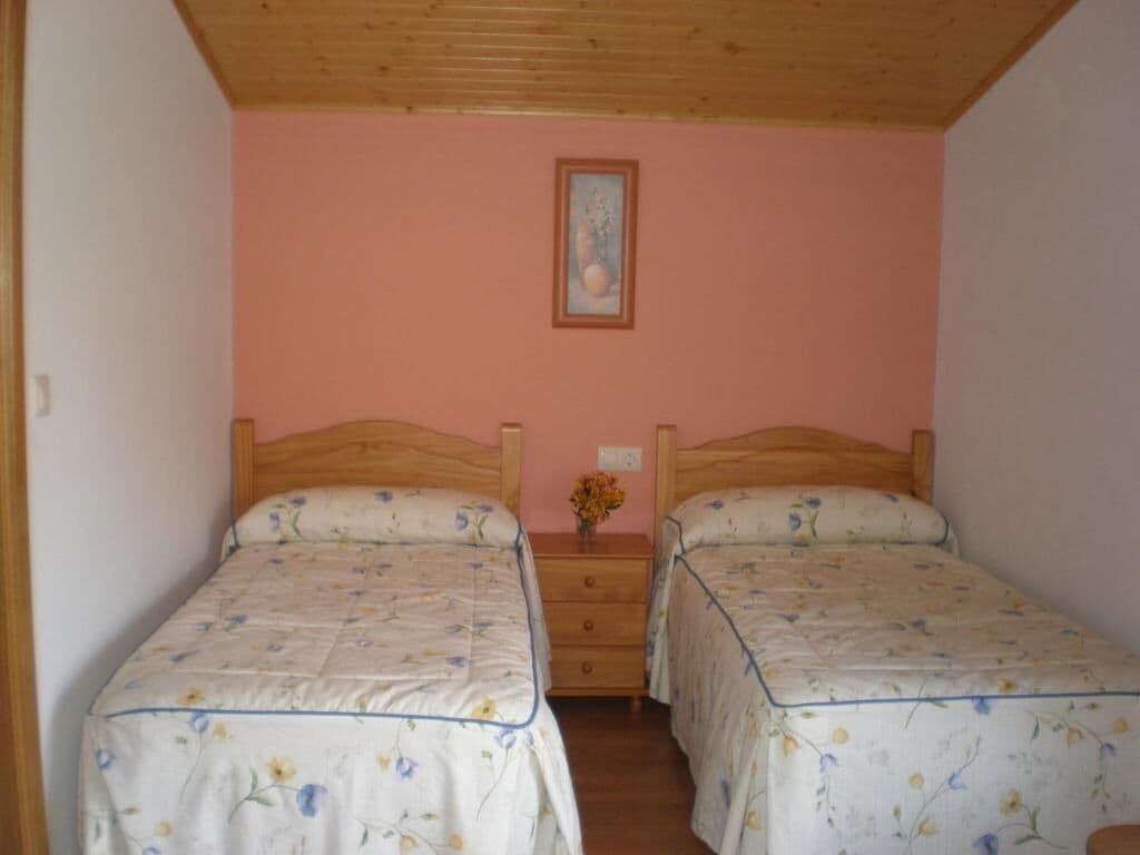 Un dormitorio con dos camas, cabeceras de madera, una pared rosa y una mesita con un florero.