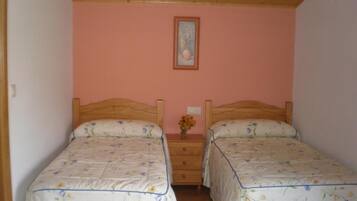 Un dormitorio con dos camas, cabeceras de madera, una pared rosa y una mesita con un florero.