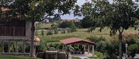 A gazebo with a red roof, surrounded by greenery and a stone bench.