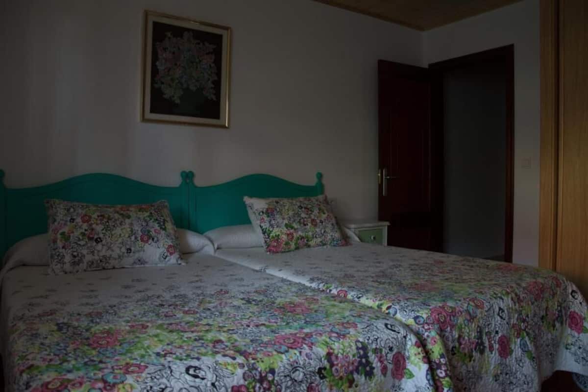 A bedroom with a bed, floral bedspread, and a framed picture on the wall.
