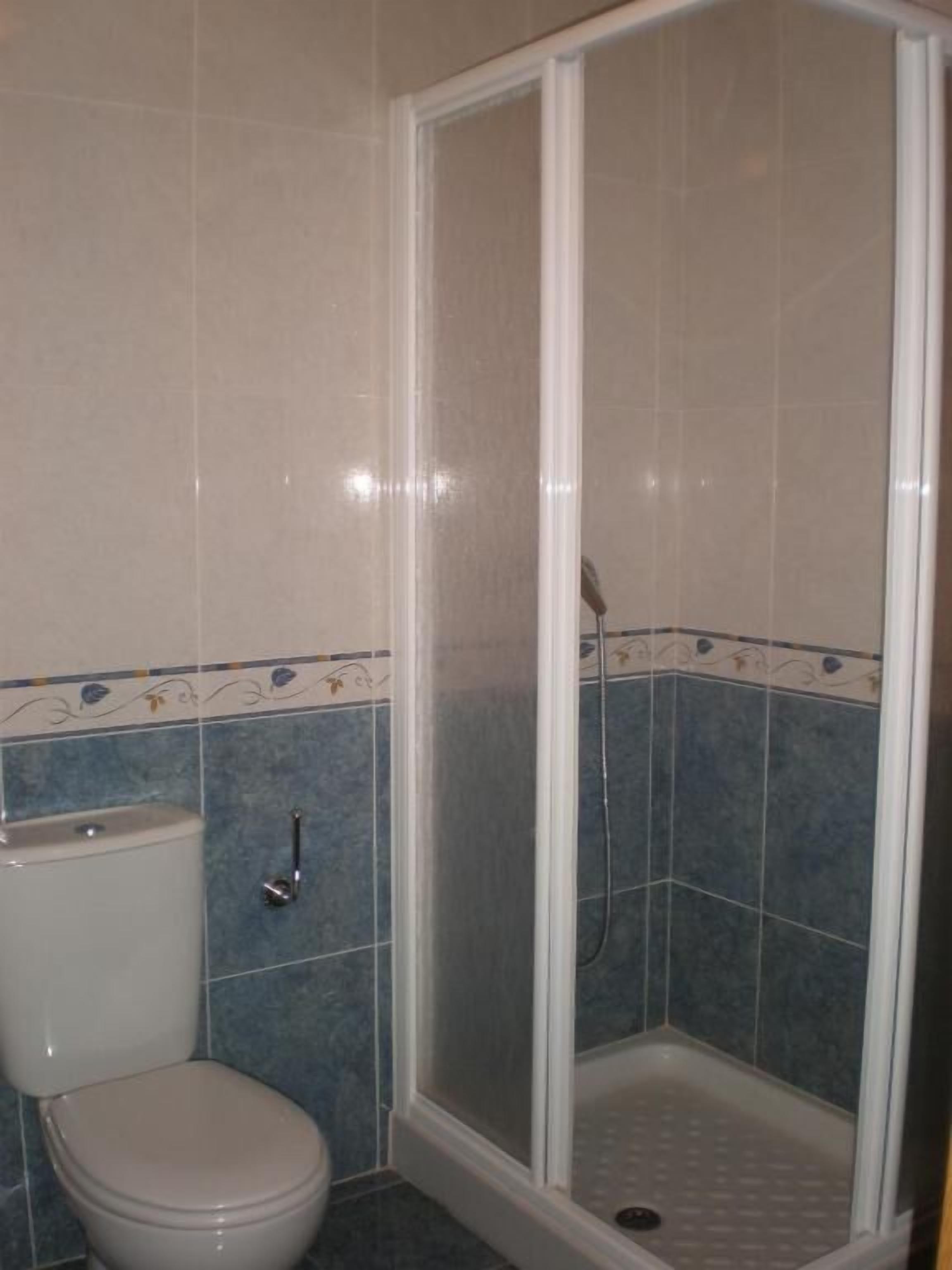 Un baño con inodoro, cabina de ducha y paredes con azulejos azules.