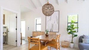 Un espace repas comprenant une table et des chaises en bois, un luminaire suspendu et une grande fenêtre donnant sur un paysage verdoyant.