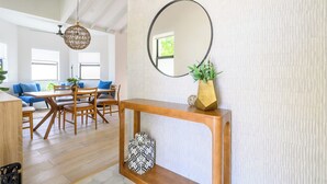 Un coin repas avec une table et des chaises en bois, un miroir rond posé sur une console, et un luminaire suspendu.