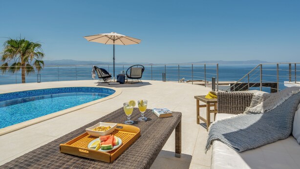 A poolside area with a view of the sea, a lounge chair, a table with drinks and snacks, and a wicker sofa. - Villa Hemera (Chania)