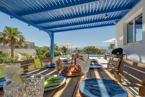 An outdoor dining area with a blue pergola, a pool, and a grill. - Villa Hemera (Chania)