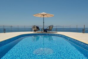 A swimming pool with two chairs and an umbrella, surrounded by a metal railing. - Villa Hemera (Chania)