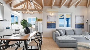 A modern kitchen with a dining area, a grey sofa, and artwork on the walls. - Villa Hemera (Chania)