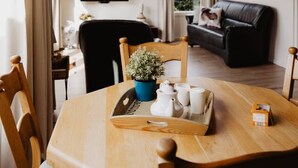 Un coin repas avec une table en bois, des chaises, un luminaire suspendu, une plante en pot et un plateau avec des tasses et une théière.
