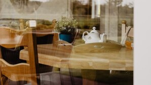 Un coin repas avec une table en bois, des chaises, une plante en pot et une théière blanche.