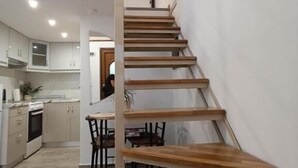 A modern kitchen with wooden flooring, a dining area with a table and chairs, and a staircase with wooden steps. - Isidora Apartments (Zagora-Mouresi)